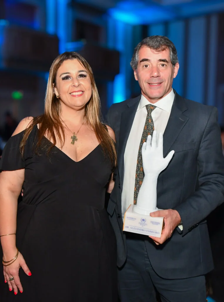 Médico premiado sostiene la estatuilla en forma de mano del Reconocimiento a la Ciencia y la Salud del Uruguay junto a una invitada durante la cena de gala